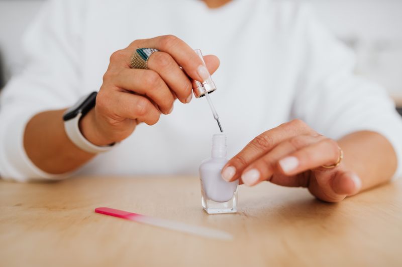 A pale lilac shade being brushed onto a nail