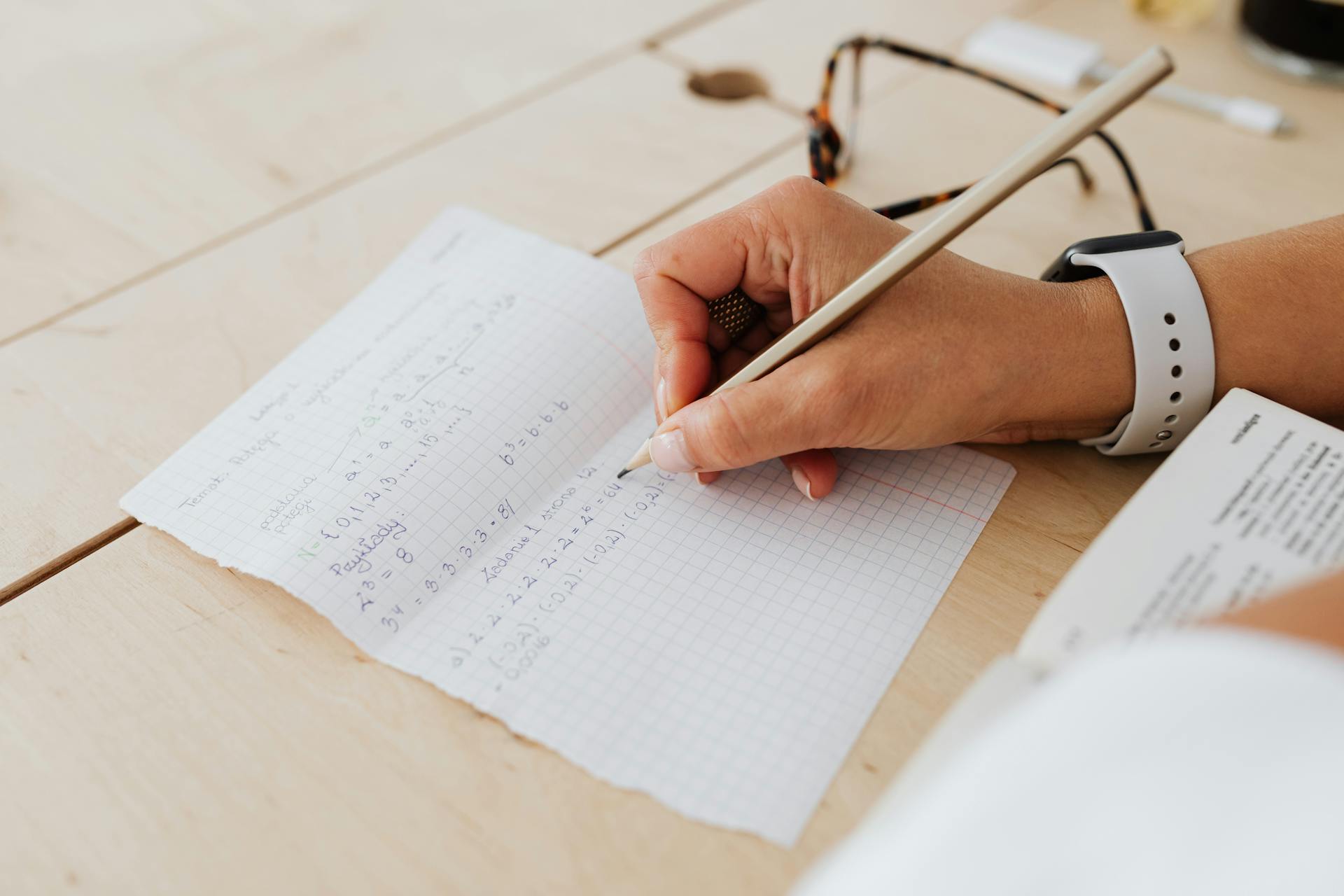 A close-up of a person writing mathematical equations on graph paper with a pencil.