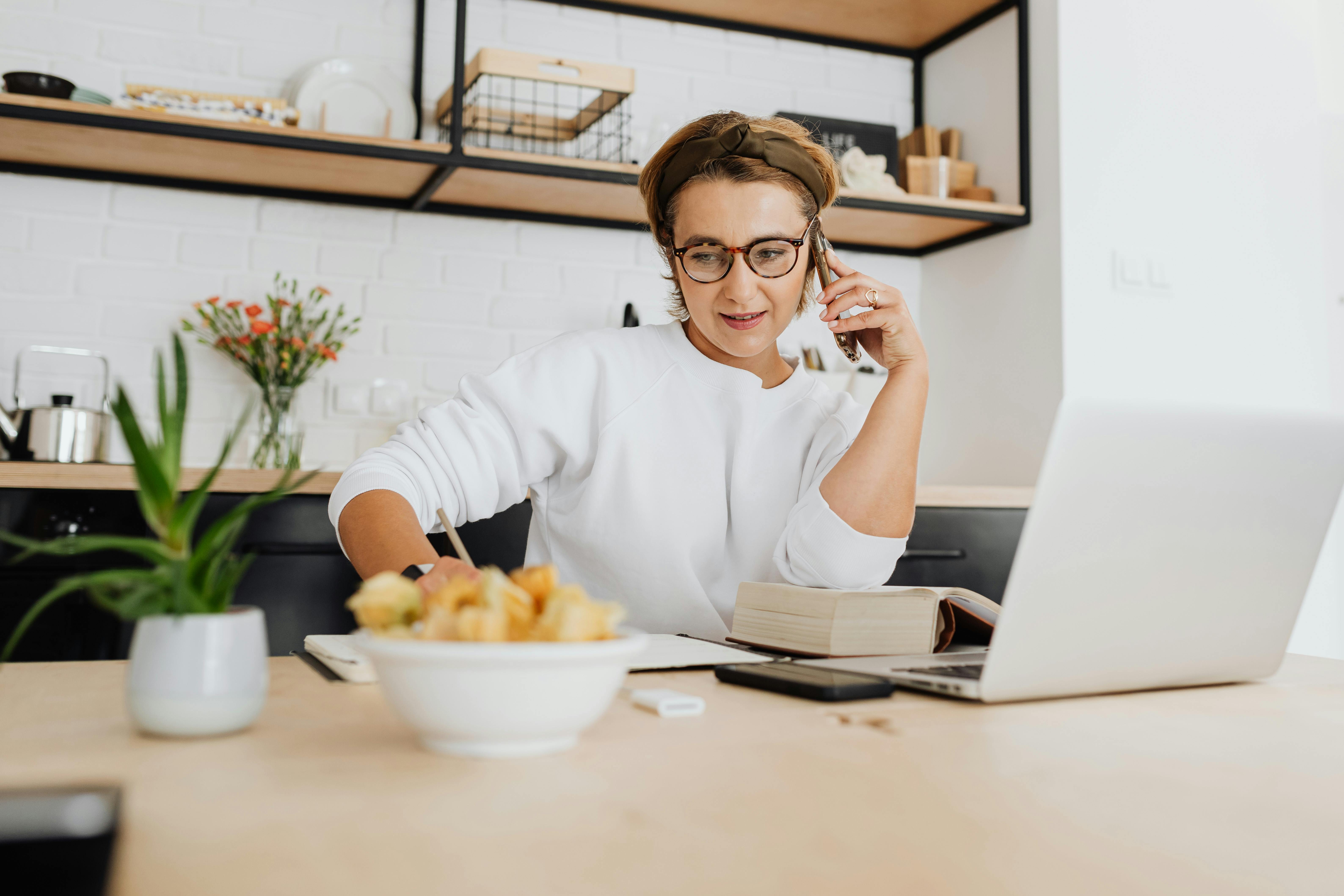 Adult woman in a white sweatshirt working from home office with laptop and phone, in a stylish kitchen. - Photo by Karolina Grabowska www.kaboompics.com on Pexels