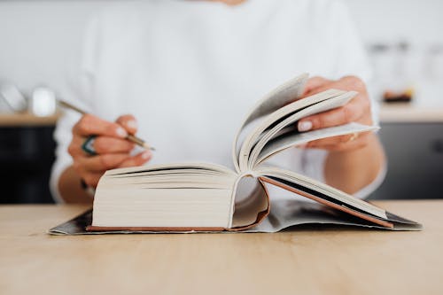 Person Holding White Book Pages and a Pen 