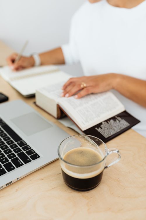 Free A woman writing in a notebook with coffee and laptop on a wooden desk. Stock Photo