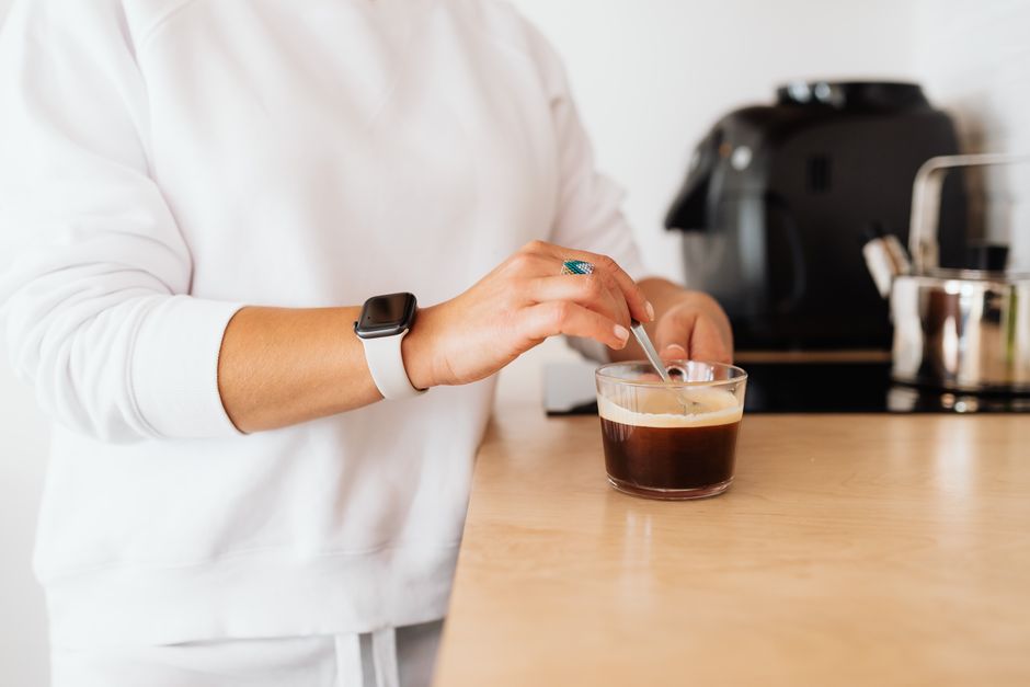 A person stirring coffee in a clear glass wearing a smartwatch, creating a cozy morning vibe.