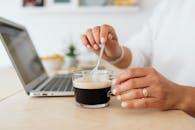 特写镜头中，一只手正用笔记本电脑搅拌咖啡，展现了休闲的工作环境