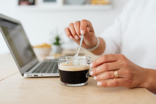 特写镜头中，一只手正用笔记本电脑搅拌咖啡，展现了休闲的工作环境