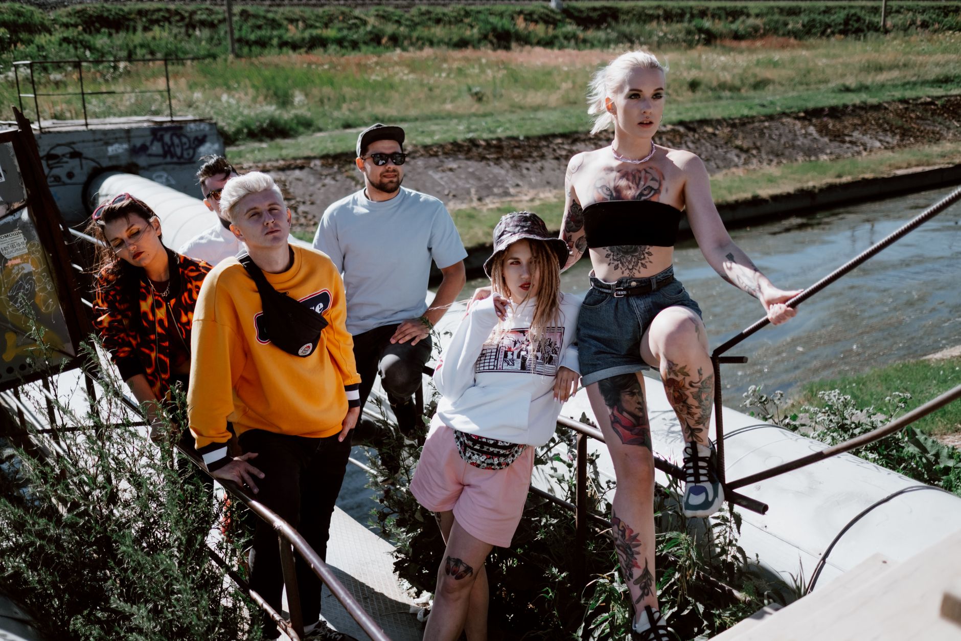 A fashionable group of adults posing confidently in streetwear by an urban canal.
