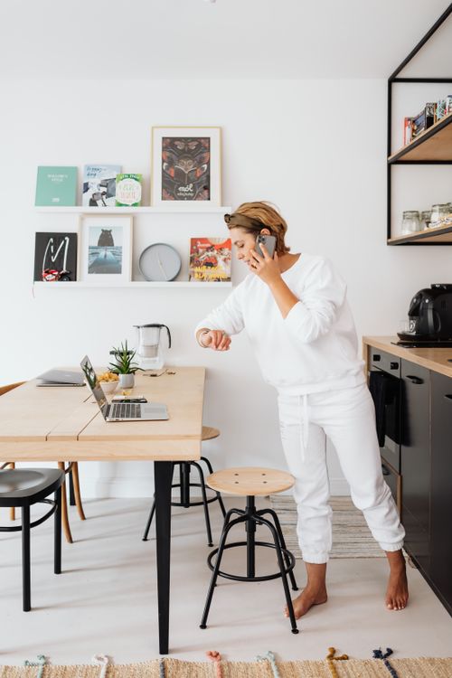Free Adult woman multitasking at home with a laptop and phone call in a modern kitchen setting. Stock Photo