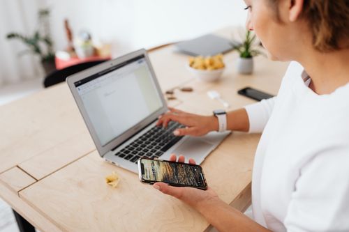 Free A woman sitting at a wooden table using a laptop and smartphone indoors. Stock Photo