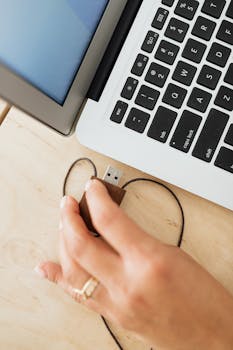 Close-up of a hand inserting a USB into a laptop, showcasing technology use in a workspace.