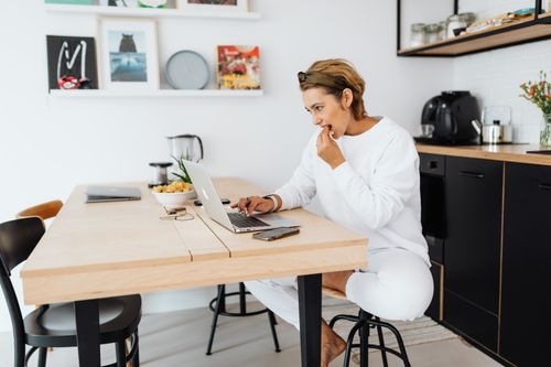 Free Casually dressed woman working on a laptop at home in a modern kitchen setting. Stock Photo