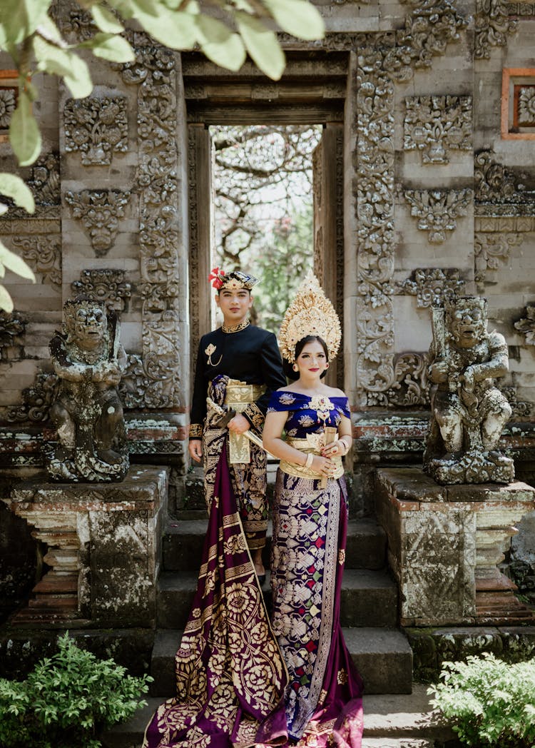 Asian Couple In Bright Ornamental Outfit On Stairs Near Sculptures