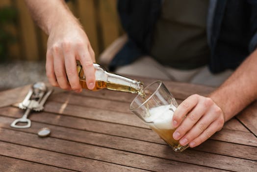 Close-up of a man's hands pouring lager beer into a glass at an outdoor wooden table. Relaxing leisure moment.