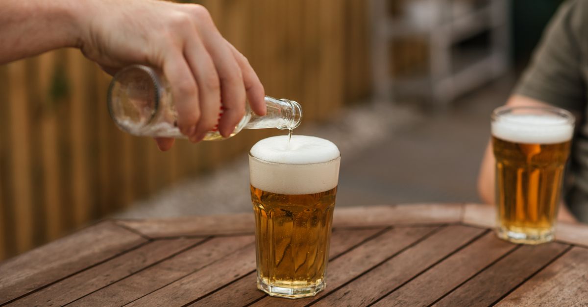 Crop anonymous male pouring beer into glass from bottle while relaxing with friend in backyard