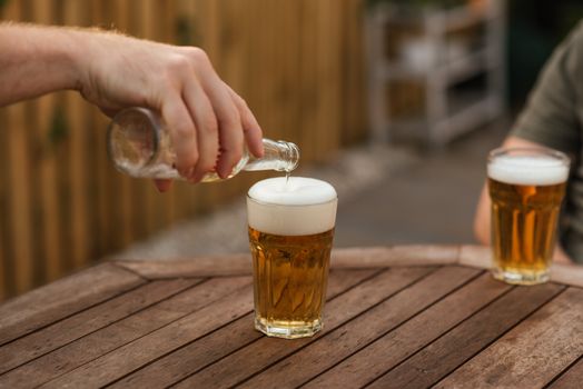 一名匿名男性在后院与朋友放松时，将啤酒从瓶子倒进玻璃杯