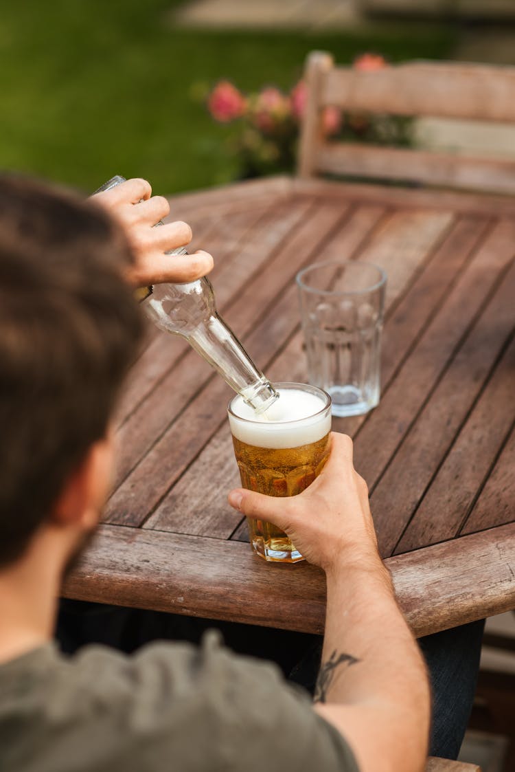 Male Pouring Beer From Bottle Into Glassware