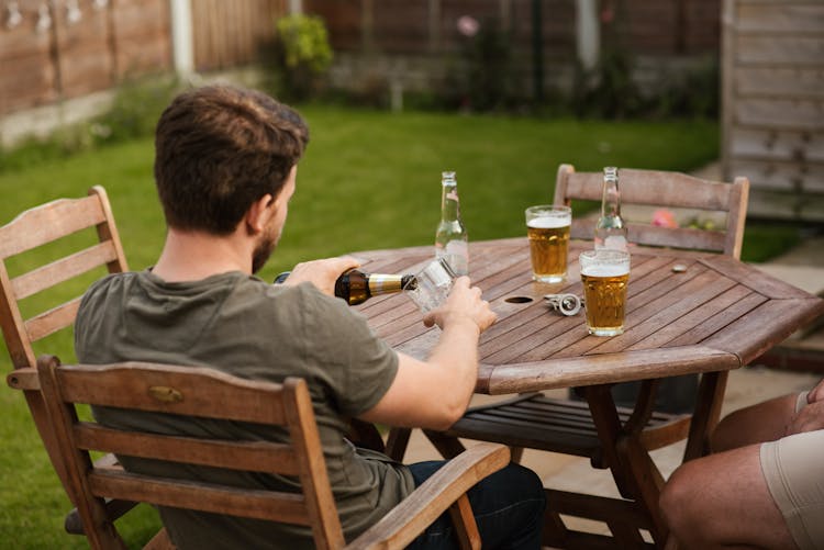 Man Pouring Beer Into Glass Mug At Table With Friend