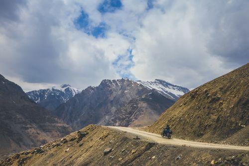 Free Scenic view of a motorcycle journey on Komic road amidst snow-capped mountains under a cloudy sky. Stock Photo