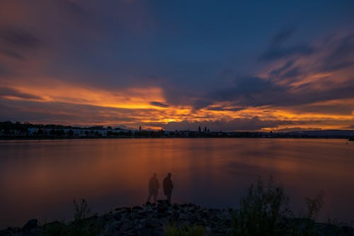 Silhouette of Person Standing on Rock Near Body of Water during Sunset