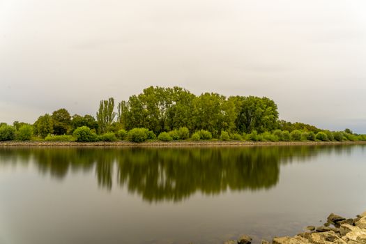 Tranquil river scene with lush trees reflecting on calm water under a cloudy sky.