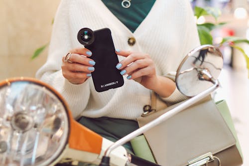 A Woman Sitting on the Motorcycle Holding a Smartphone with Black Case