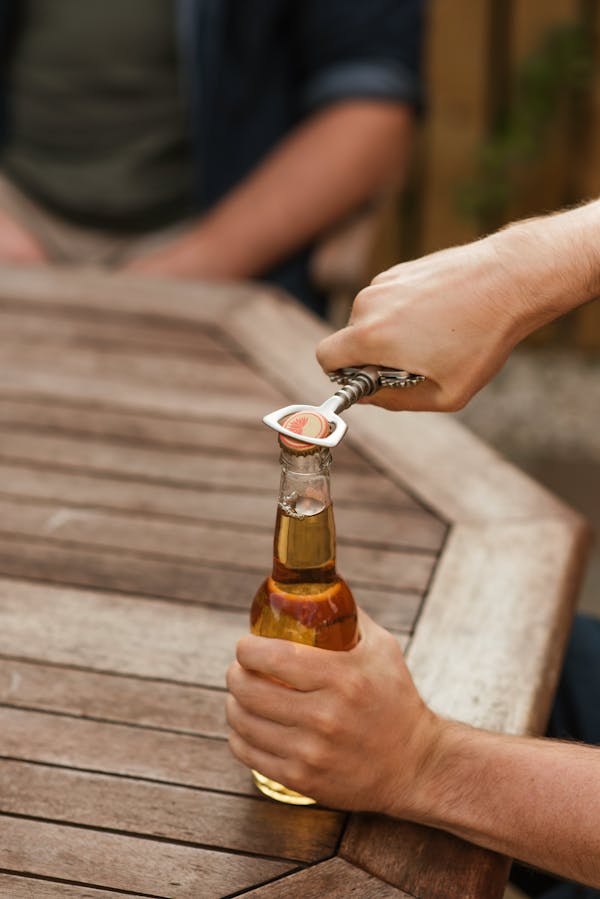 Man taking off cap of beer bottle with opener