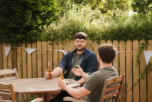 Male friends drinking beer at table in backyard