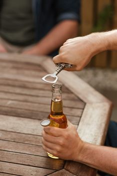一位匿名男性在空闲时与朋友一起打开一瓶啤酒，地点在农作物上方