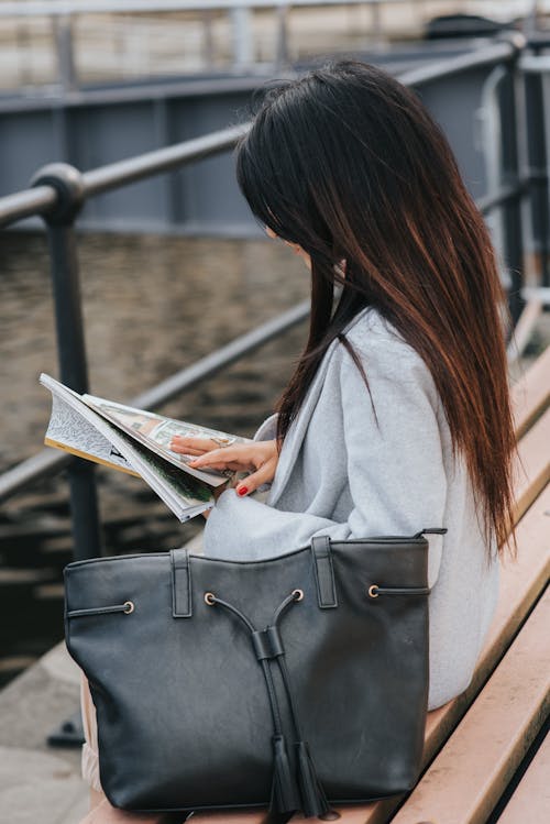 街のウォーターフロントのベンチで雑誌を読む女性