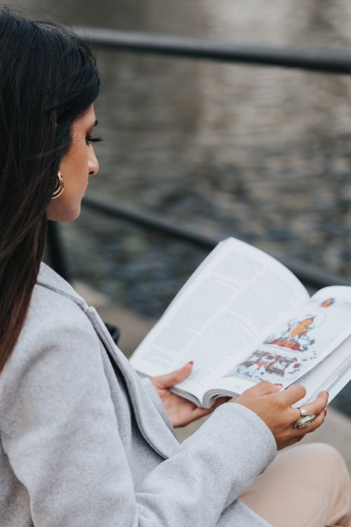 Free High angle side view of focused female reading literature while resting on city embankment Stock Photo