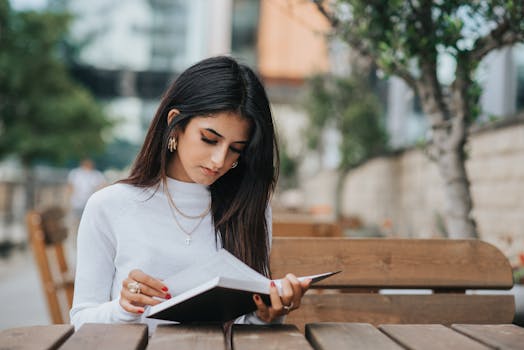 一名年轻女子若有所思地坐在户外木凳上读书