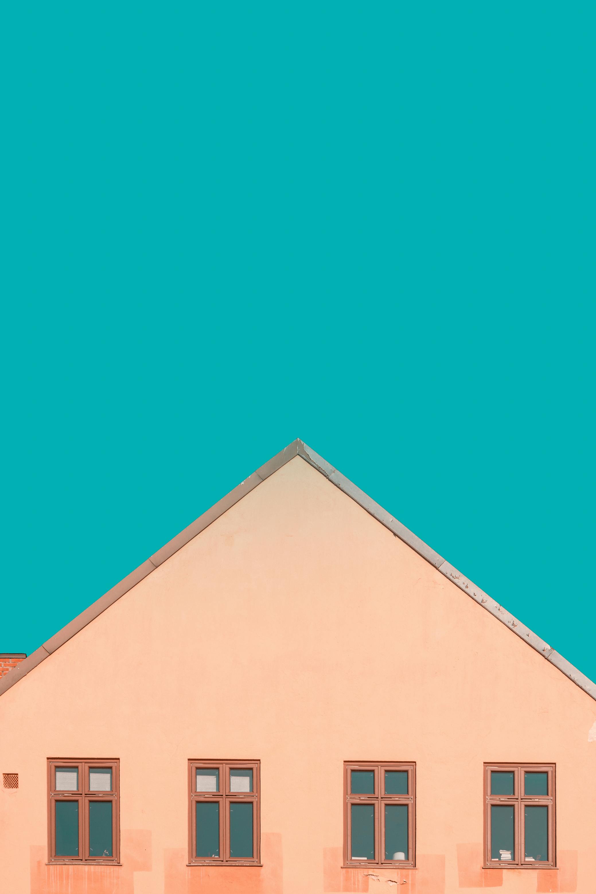 Peach house facade with triangular roof against a vivid teal sky in Oslo.