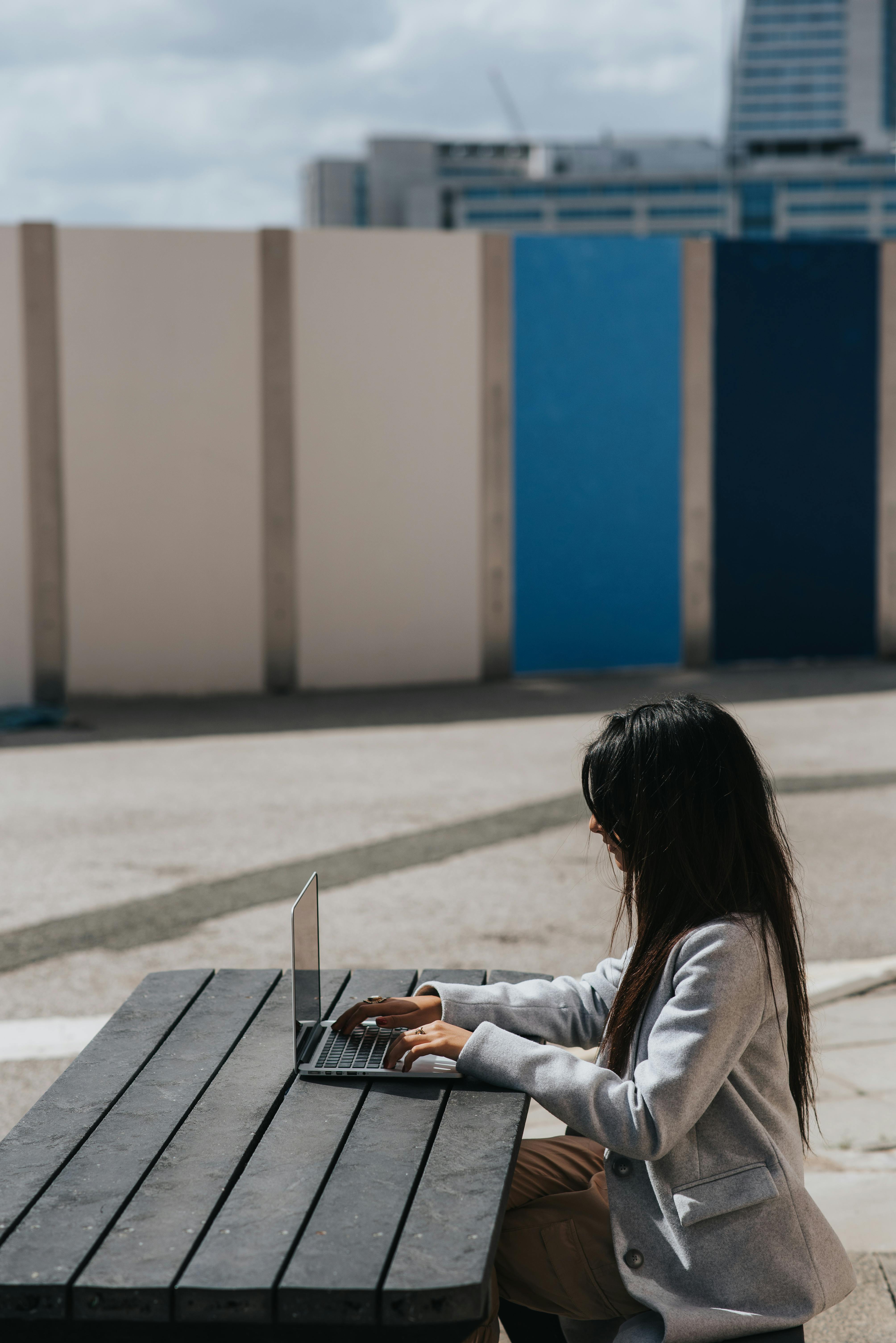 unrecognizable ethnic businesswoman typing on laptop at street table