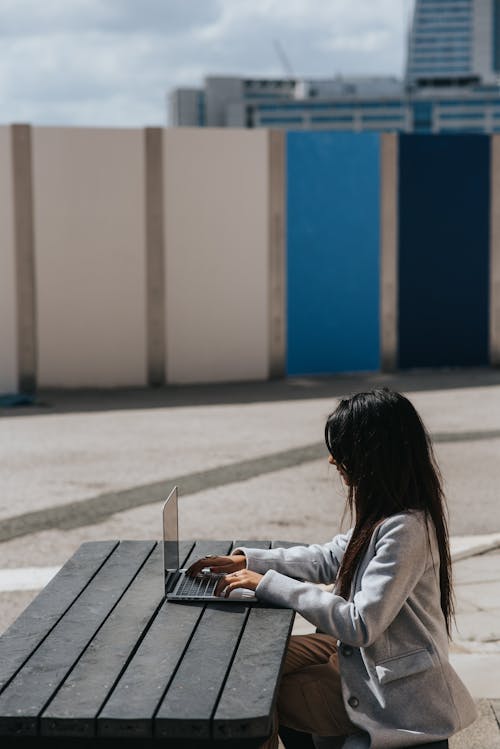 Free Side view of anonymous ethnic female freelancer working on netbook at wooden table in town Stock Photo