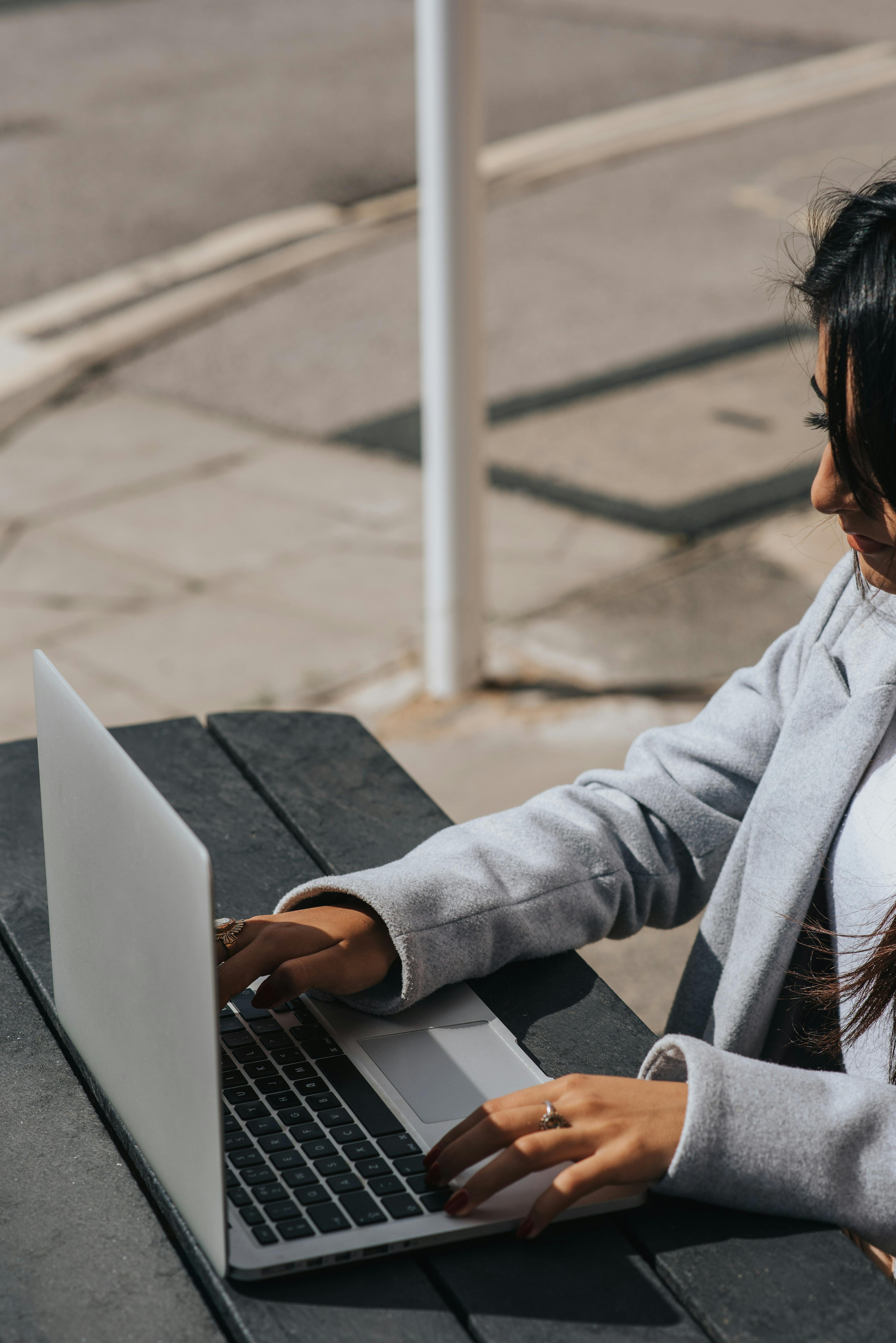 crop ethnic freelancer typing on laptop at street table