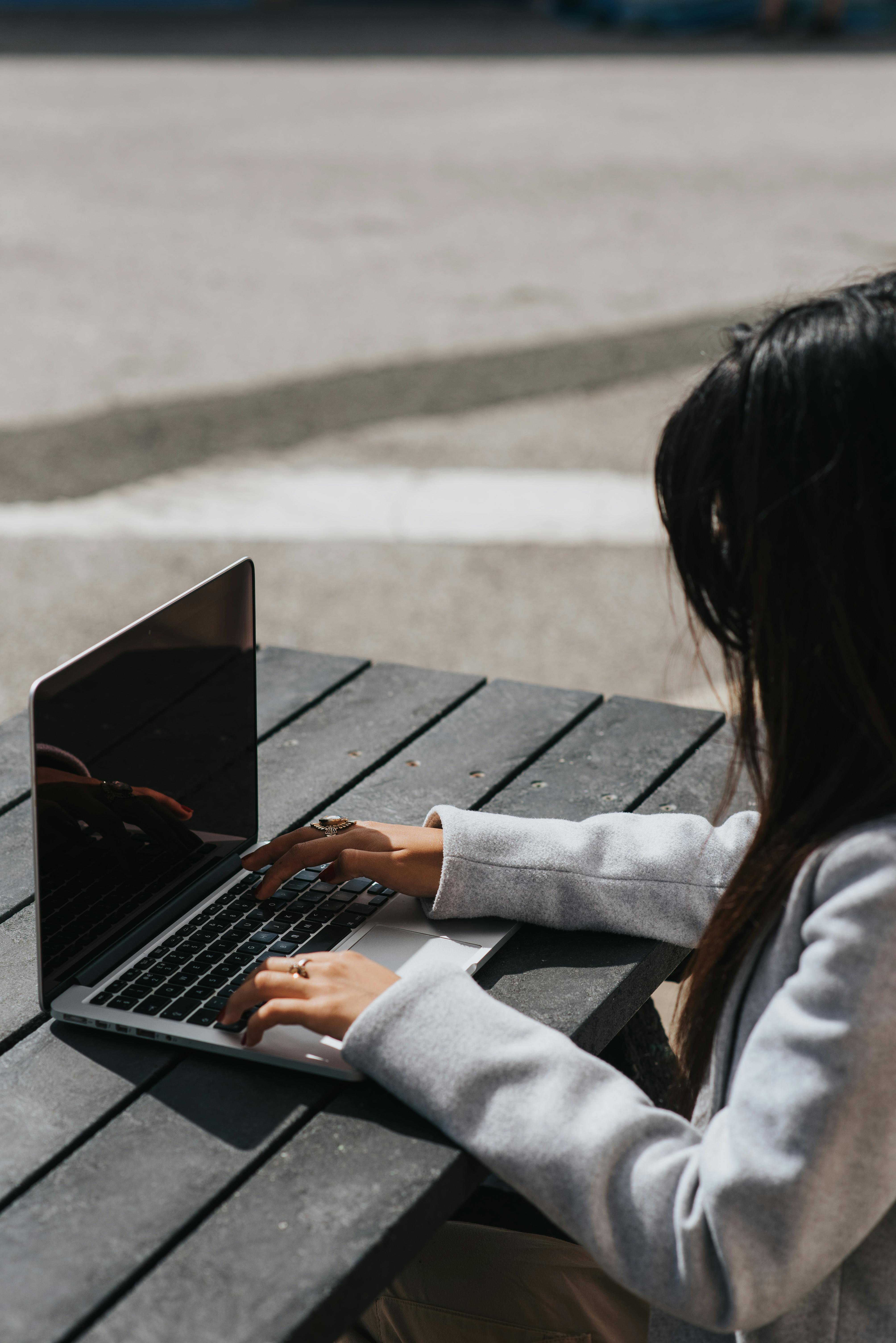 unrecognizable businesswoman working on laptop at table in city