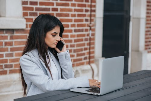 Dizüstü Bilgisayarda çalışırken Akıllı Telefonda Konuşan Ciddi Etnik Girişimci