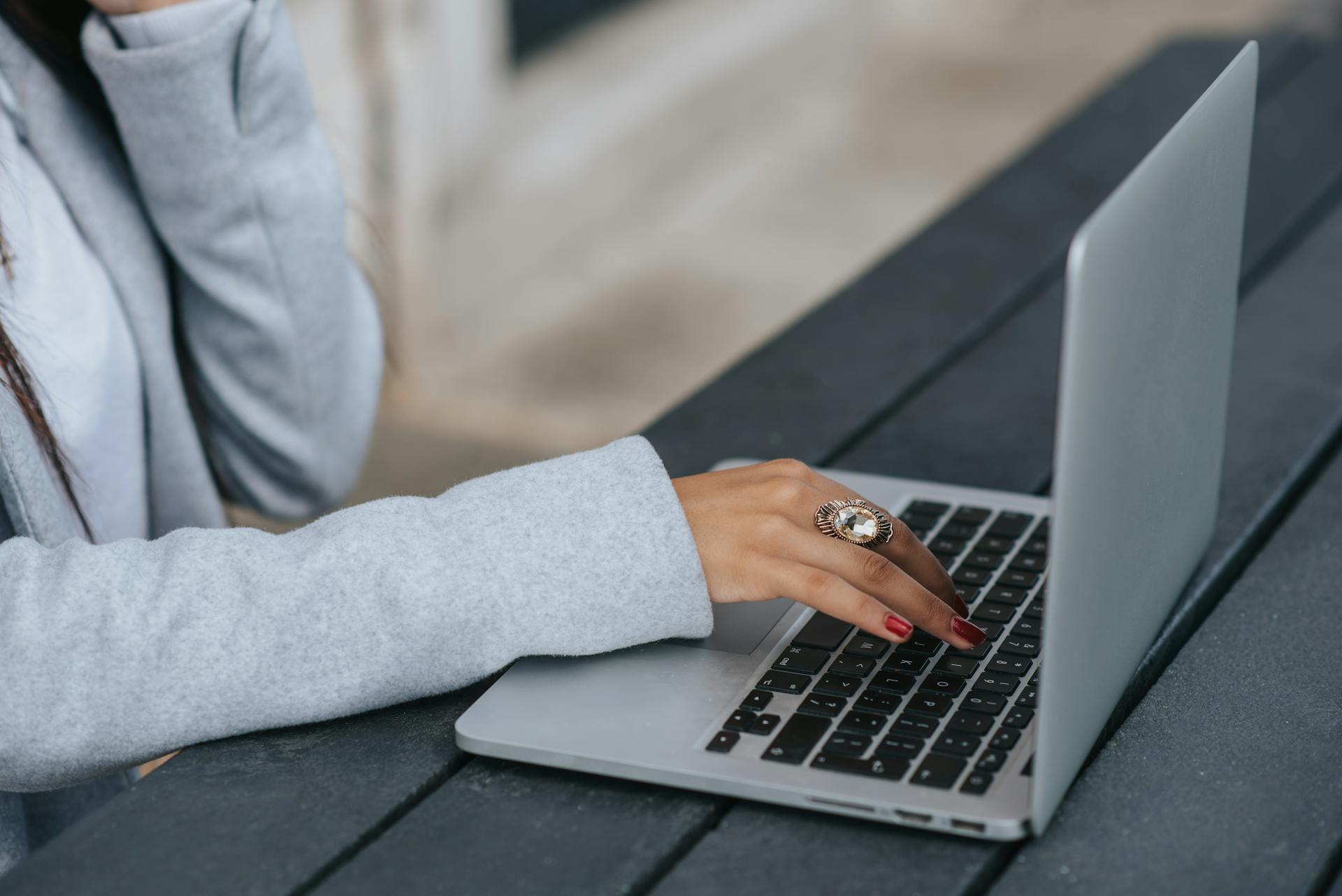 Side view of crop anonymous female entrepreneur in luxury ring working on netbook at wooden table