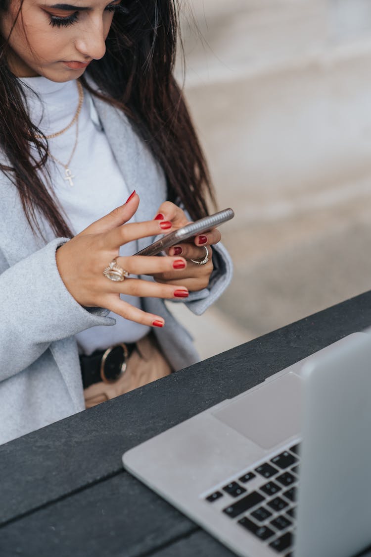 Crop Ethnic Businesswoman Chatting On Smartphone Near Laptop On Street