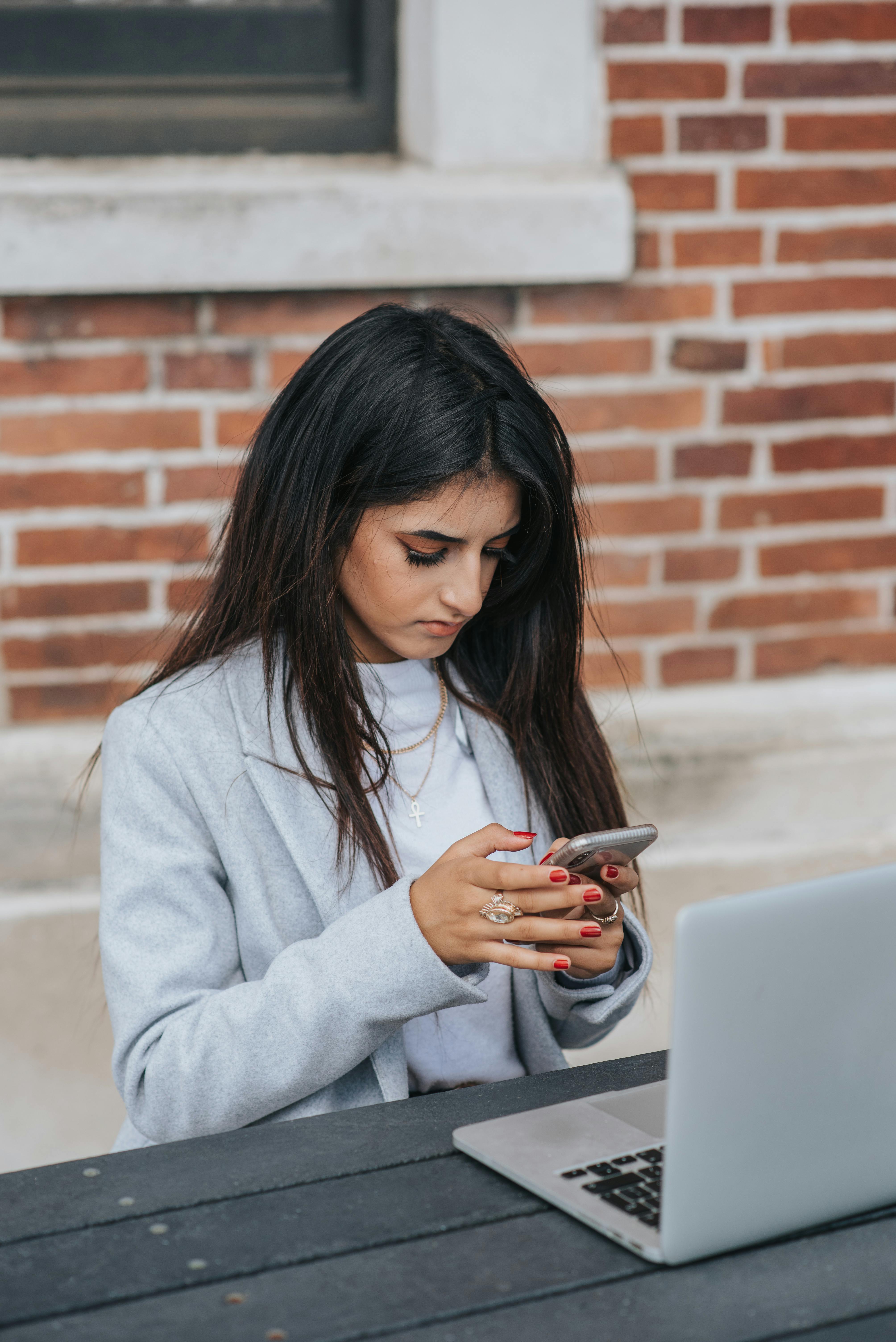 concentrated ethnic businesswoman chatting on smartphone near laptop in city