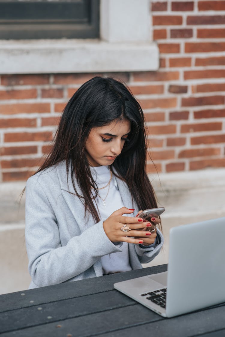 Concentrated Ethnic Businesswoman Chatting On Smartphone Near Laptop In City