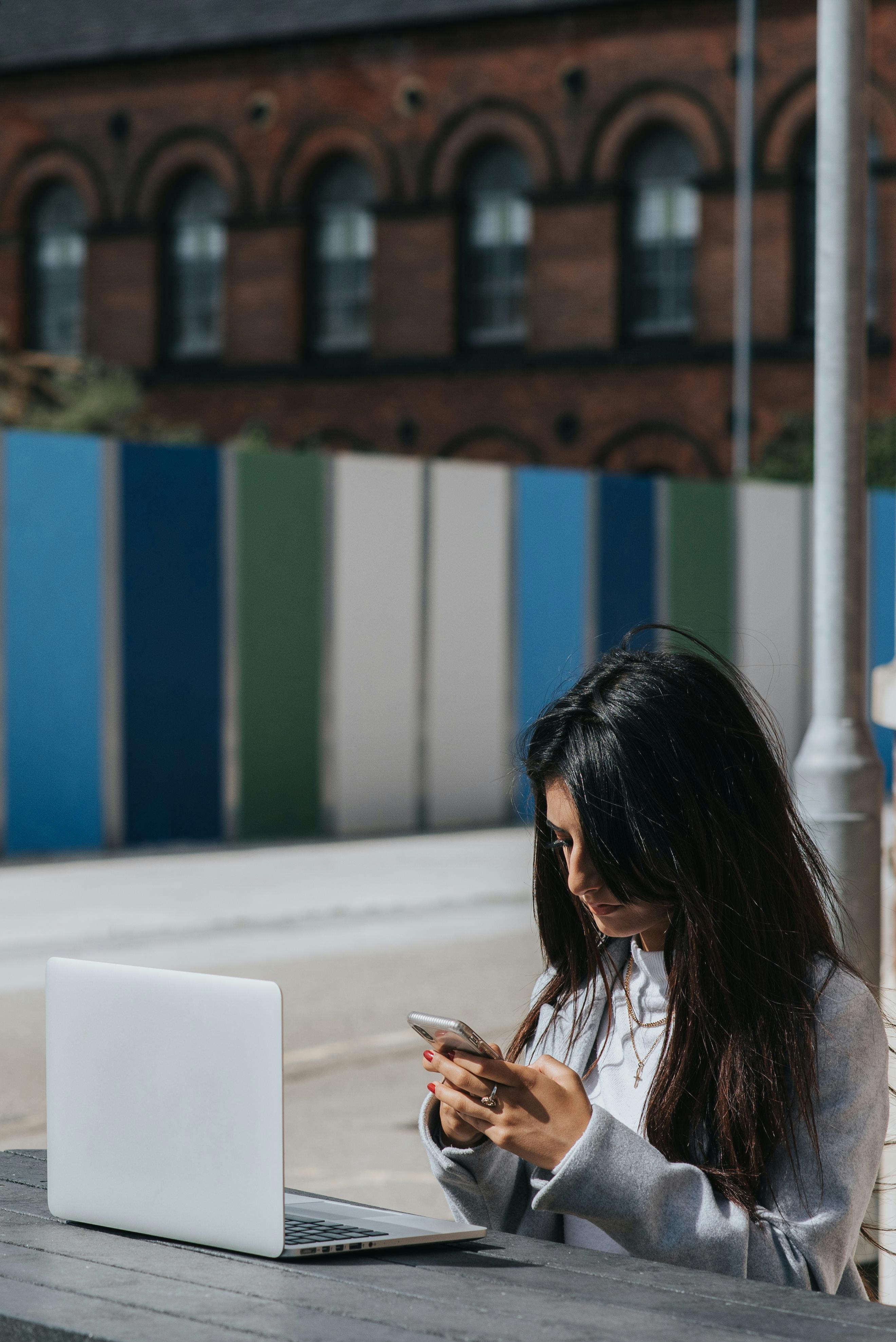 ethnic female entrepreneur chatting on smartphone at table with laptop