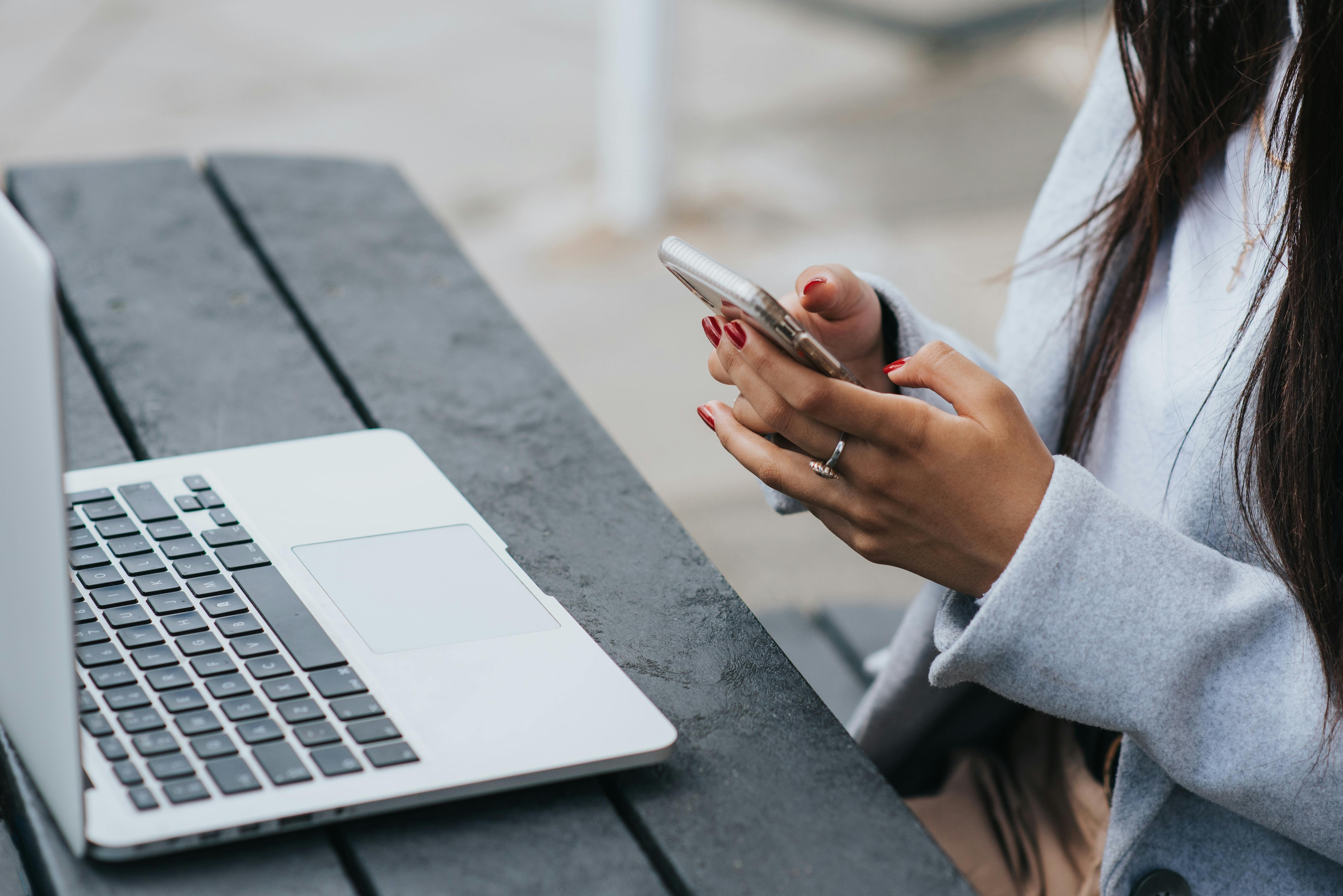 crop ethnic businesswoman chatting on smartphone near laptop on table