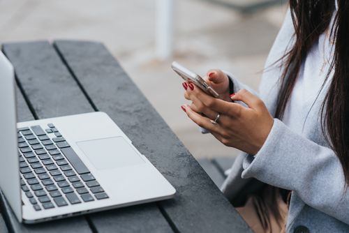 Free From above side view of faceless ethnic female manager text messaging on cellphone near netbook on street table Stock Photo