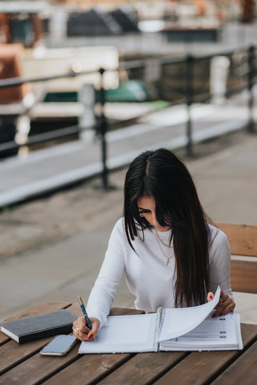 Free Focused ethnic employee taking notes in notepad at street table Stock Photo