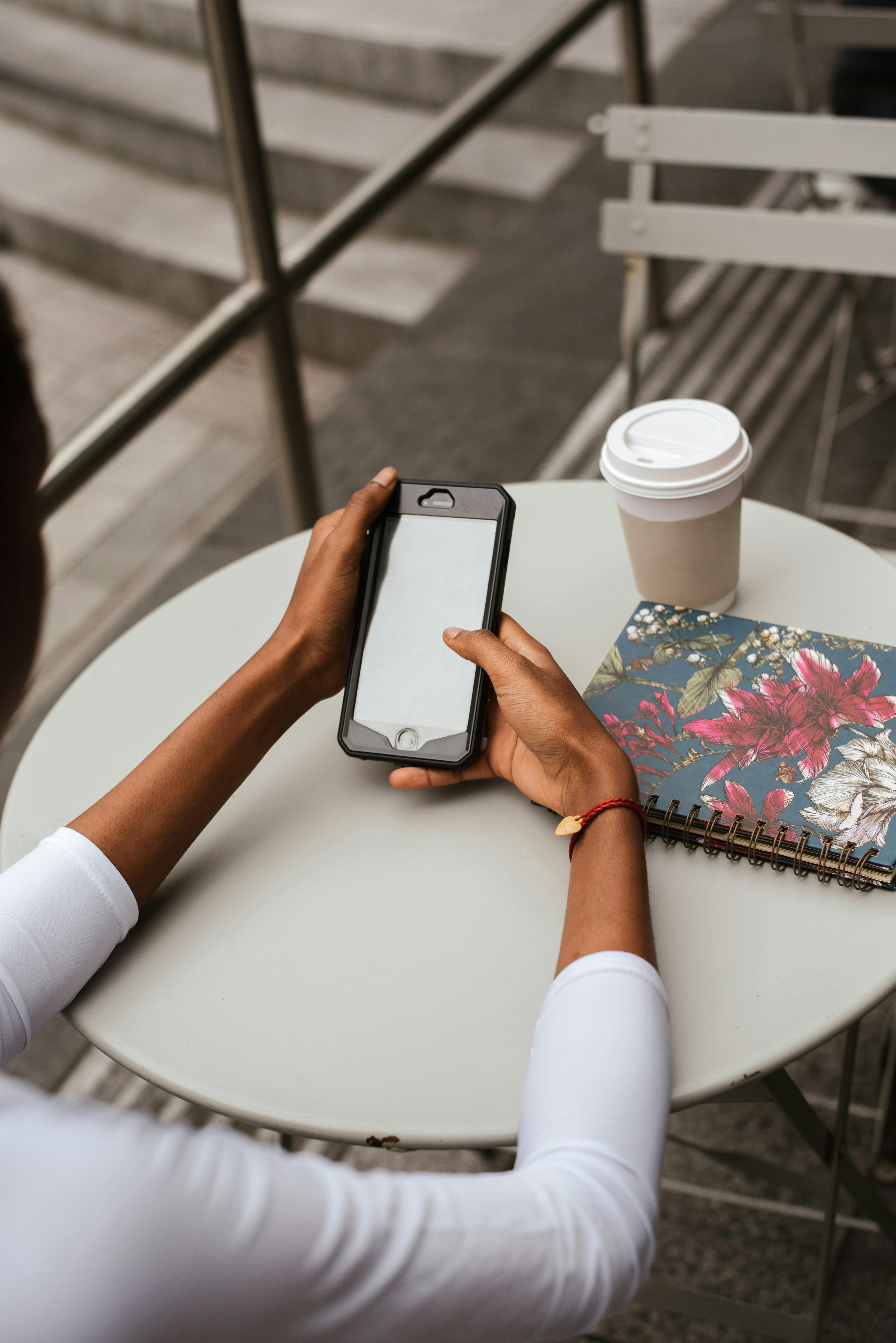 unrecognizable ethnic woman surfing internet on smartphone at cafeteria table