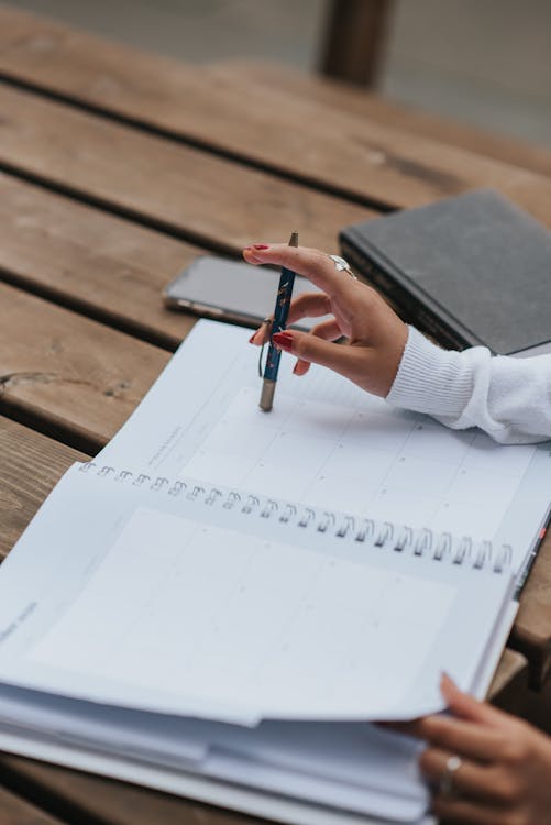 Free From above of crop anonymous ethnic female entrepreneur with pen and notebook working at wooden table Stock Photo