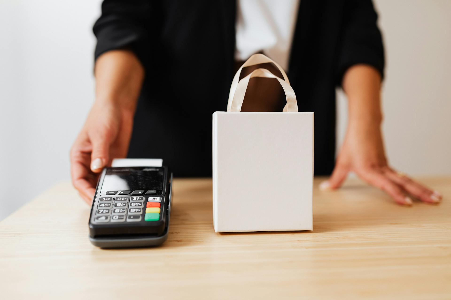 Person Holding Black Payment Terminal beside White Paper Bag