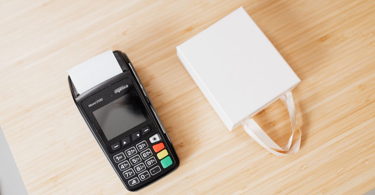 A payment terminal and a small white gift bag on a wooden countertop, ideal for commerce themes.