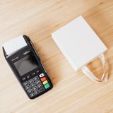 A payment terminal and a small white gift bag on a wooden countertop, ideal for commerce themes.