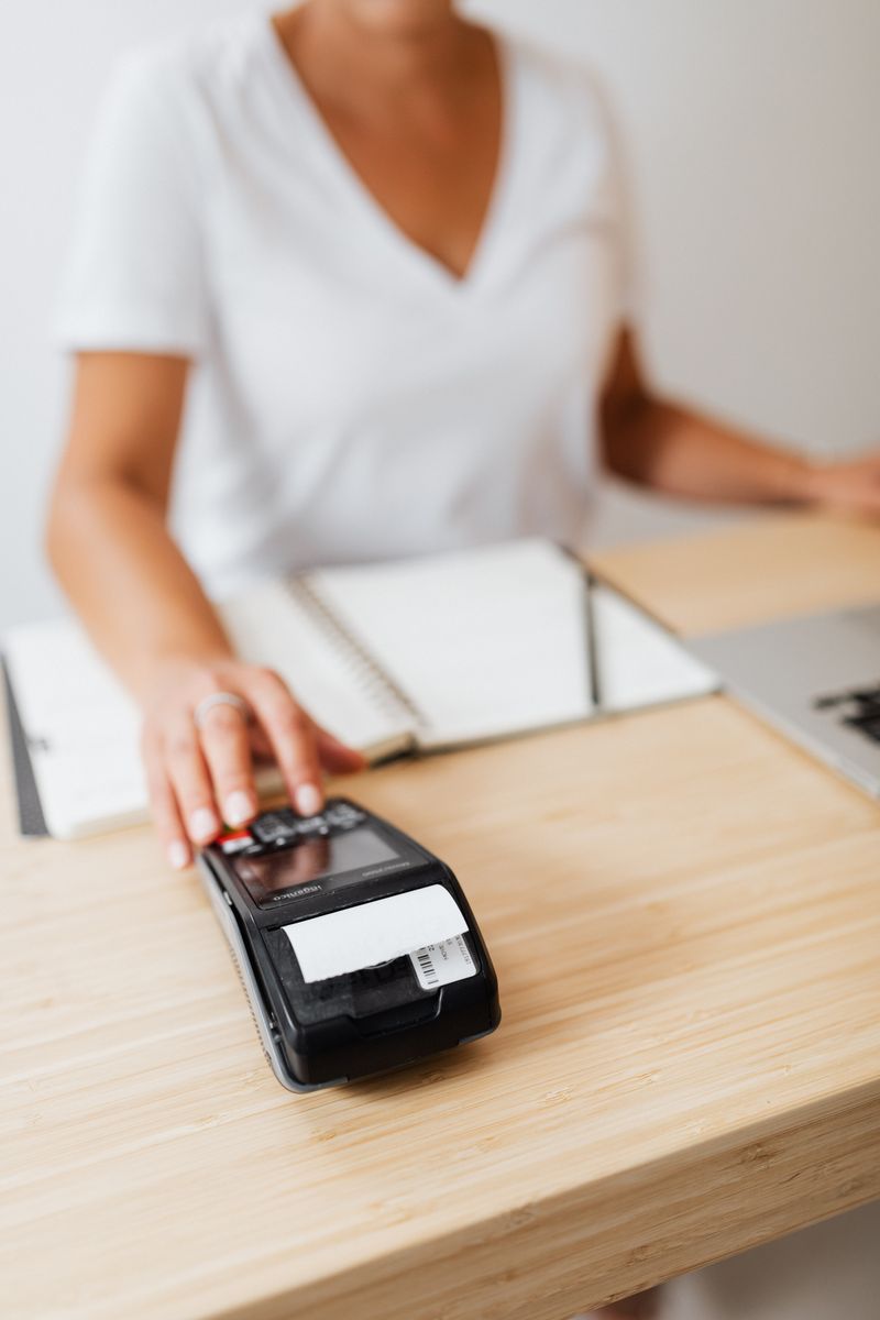 A person makes a cashless payment using a terminal on a desk, illustrating modern payment methods.