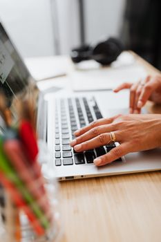 Hands with rings typing on a laptop keyboard in a bright workspace.